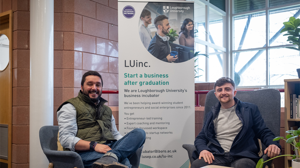 Alex and Andreas sitting at a coffee table in front of an LUinc. banner smiling. 